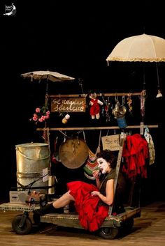 a woman in a red dress sitting on top of a cart with an umbrella over her head