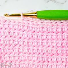 a crocheted pink and green blanket with a gold colored metal ballpoint pen resting on it