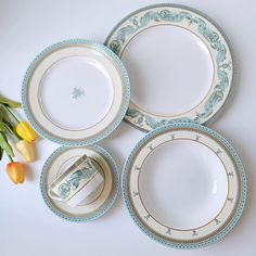 three plates and two cups with tulips in the background on a white surface