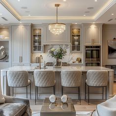 an elegant kitchen and living room with marble counter tops, white cabinets, gray velvet chairs, and gold chandelier