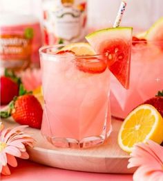 two glasses filled with watermelon and lemonade next to strawberries on a cutting board