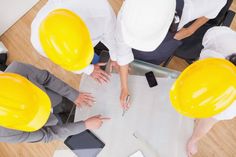 three people in hardhats looking down at a blueprint on a table with construction equipment