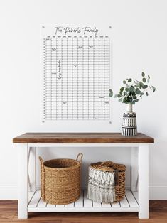 a wooden table with two baskets and a calendar on the wall above it, in front of a white wall