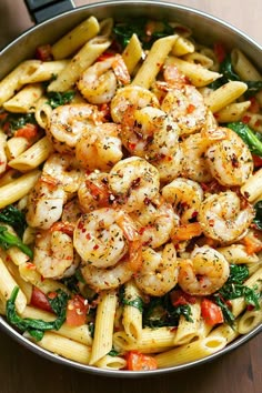 pasta with shrimp, spinach and tomatoes in a skillet on a wooden table