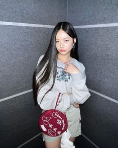 a woman standing in front of a gray wall holding a red and white mickey mouse bag