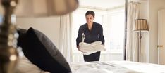 a woman standing in front of a bed with white sheets and pillows on top of it