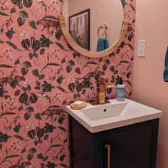 a sink and mirror in a room with pink wall paper on the walls behind it