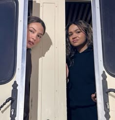 two women standing in the doorway of a bus looking out from behind them are another woman