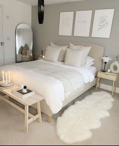 a white bed sitting in a bedroom next to a table with candles on it and pictures hanging above the bed