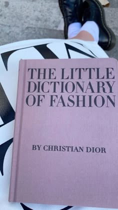 the little dictionary of fashion by christian dior is on top of a white chair