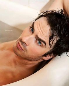 a shirtless man laying in a bathtub with blue eyes