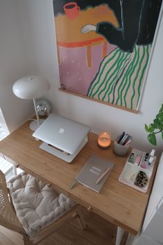 a laptop computer sitting on top of a wooden desk next to a lamp and painting