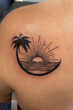 the back of a woman's shoulder with a palm tree and sun tattoo on it