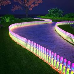 an illuminated pathway in the middle of a park at night with flowers and trees around it