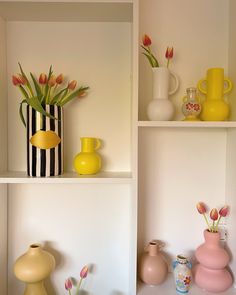 some vases and flowers are on shelves in a room with white walls or shelving