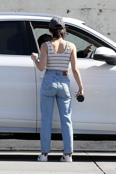 a woman standing in front of a white car with her hand on the door handle