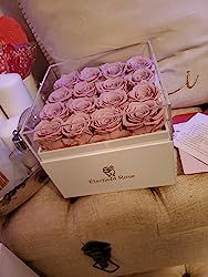 a box filled with pink roses sitting on top of a bed next to pillows and other items