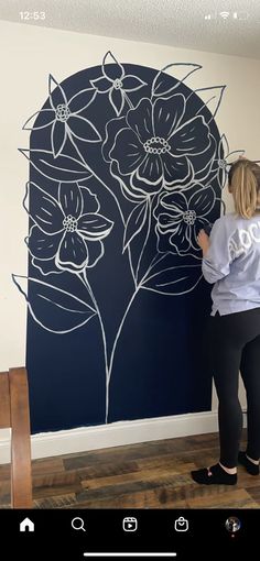 a woman standing in front of a wall with flowers painted on it