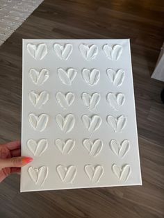 a person holding up a white paper with hearts on it in front of a wooden floor