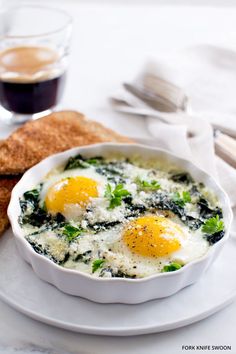 two fried eggs in a white bowl on a plate next to bread and utensils