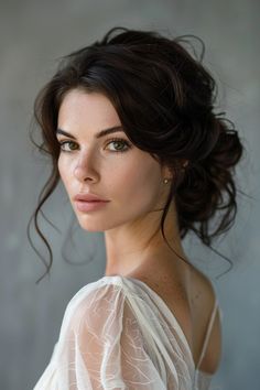 a woman with dark hair wearing a white dress and posing for a photo in front of a gray wall