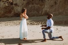 a man kneeling down next to a woman on the beach while she holds her hand near her face