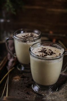 two glasses filled with white liquid sitting on top of a wooden table next to cinnamon sticks