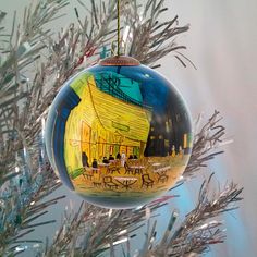 an ornament hanging from a christmas tree with a painting on it's side