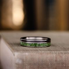 a wedding band with green marble inlays sits on top of a piece of cloth