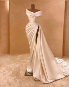 a white wedding dress on display in front of a beige wall with a mannequin behind it