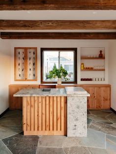 a kitchen with stone flooring and wooden cabinetry next to a large open window