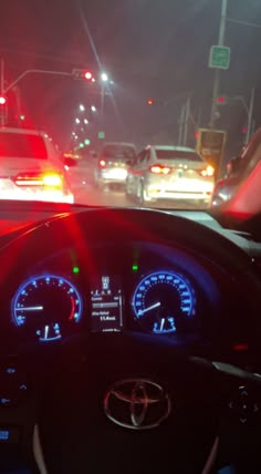 the dashboard of a car at night with lights on and cars driving in the background