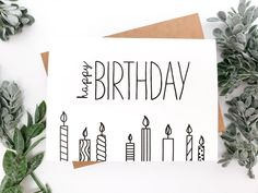 a happy birthday card with candles and plants on the table next to it, surrounded by greenery