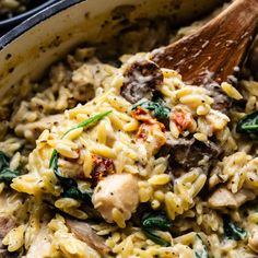 a wooden spoon in a pot filled with pasta and spinach