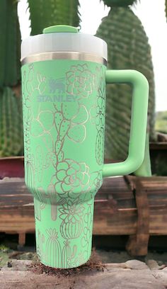 a green coffee cup sitting on top of a wooden table next to cacti