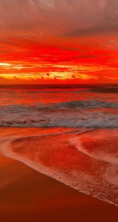 an orange and red sunset over the ocean with waves coming in to shore on a sandy beach