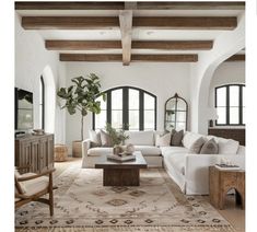 a living room with white couches and wooden beams in the ceiling, along with an area rug on the floor