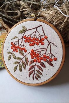 an embroidery hoop with red berries on it and some yarn in the background, along with twine of twine