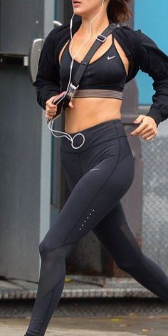 a woman in black sports bra top and leggings running on street with headphones