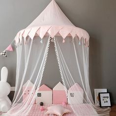 a pink bed with white netting and bunny ears on the headboard is in front of a gray wall