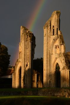 a rainbow shines brightly in the sky above an old building with stone pillars and arches