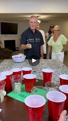 a group of people standing around a table with red cups on it and one person holding a green object