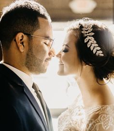 a bride and groom standing close to each other in front of a window with sunlight streaming through them