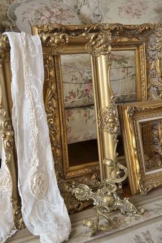 there are many ornate gold frames on the fireplace mantel, and one is holding a white lace curtain