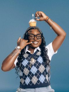 a woman holding a cupcake on top of her head while wearing glasses and a sweater vest