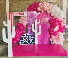 pink and white balloons are on display in front of a brick wall with cactus decorations