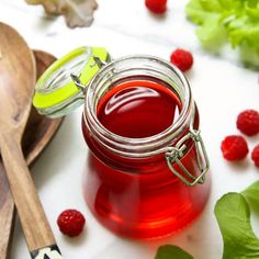 a jar filled with raspberry jam next to a wooden spoon and leafy greens