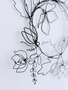 a wire sculpture with flowers and leaves hanging from it's sides on a wall