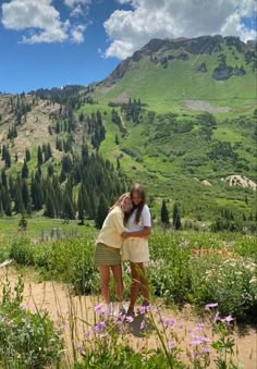 two girls standing in the middle of a field with mountains in the backgroud