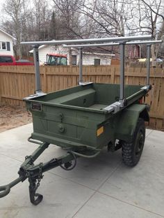 an army green utility trailer parked in front of a fence